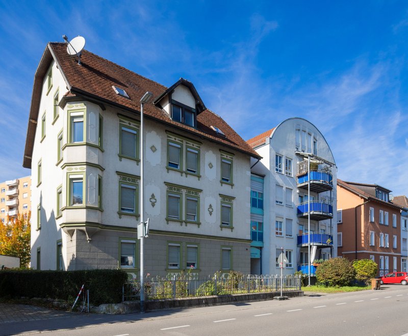 Wohnhäuser SWG Friedrichshafen Straße mit Reihen von Wohnhäusern unterschiedlicher Architektur unter blauem Himmel, von klassisch bis modern gestaltet.