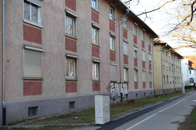 Paulinenstraße SWG Mehrere mehrstöckige Wohngebäude mit einer grauen und roten Fassade entlang einer ruhigen Straße, teilweise mit geschlossenen Rollläden an den Fenstern.